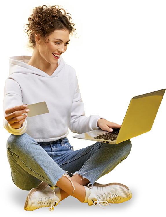 A woman sitting on the ground holding a credit card and using her laptop.